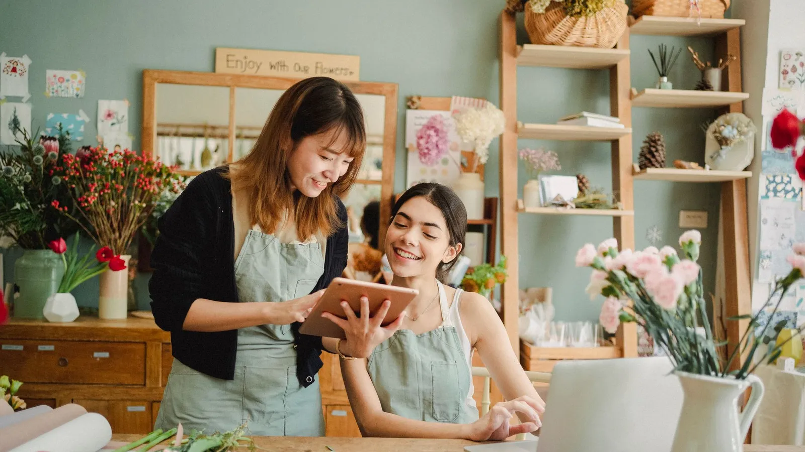 Deux créatrices préparant leur catalogue de produits sur tablette et ordinateur dans leur atelier