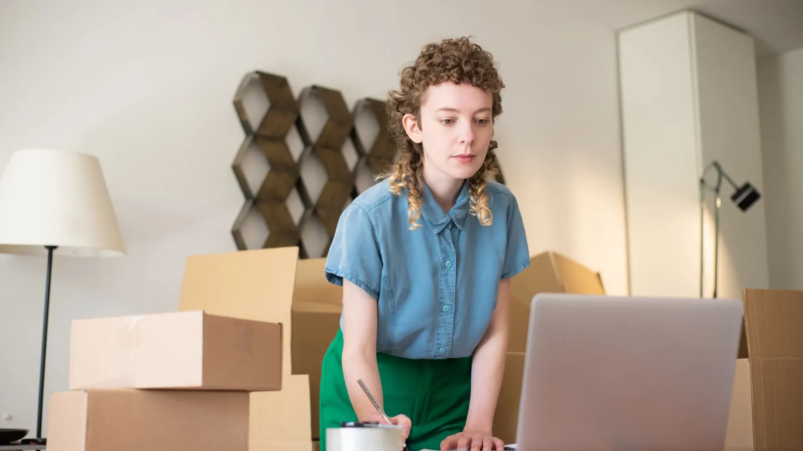 Créatrice travaillant sur son ordinateur portable au milieu des cartons de sa boutique en ligne