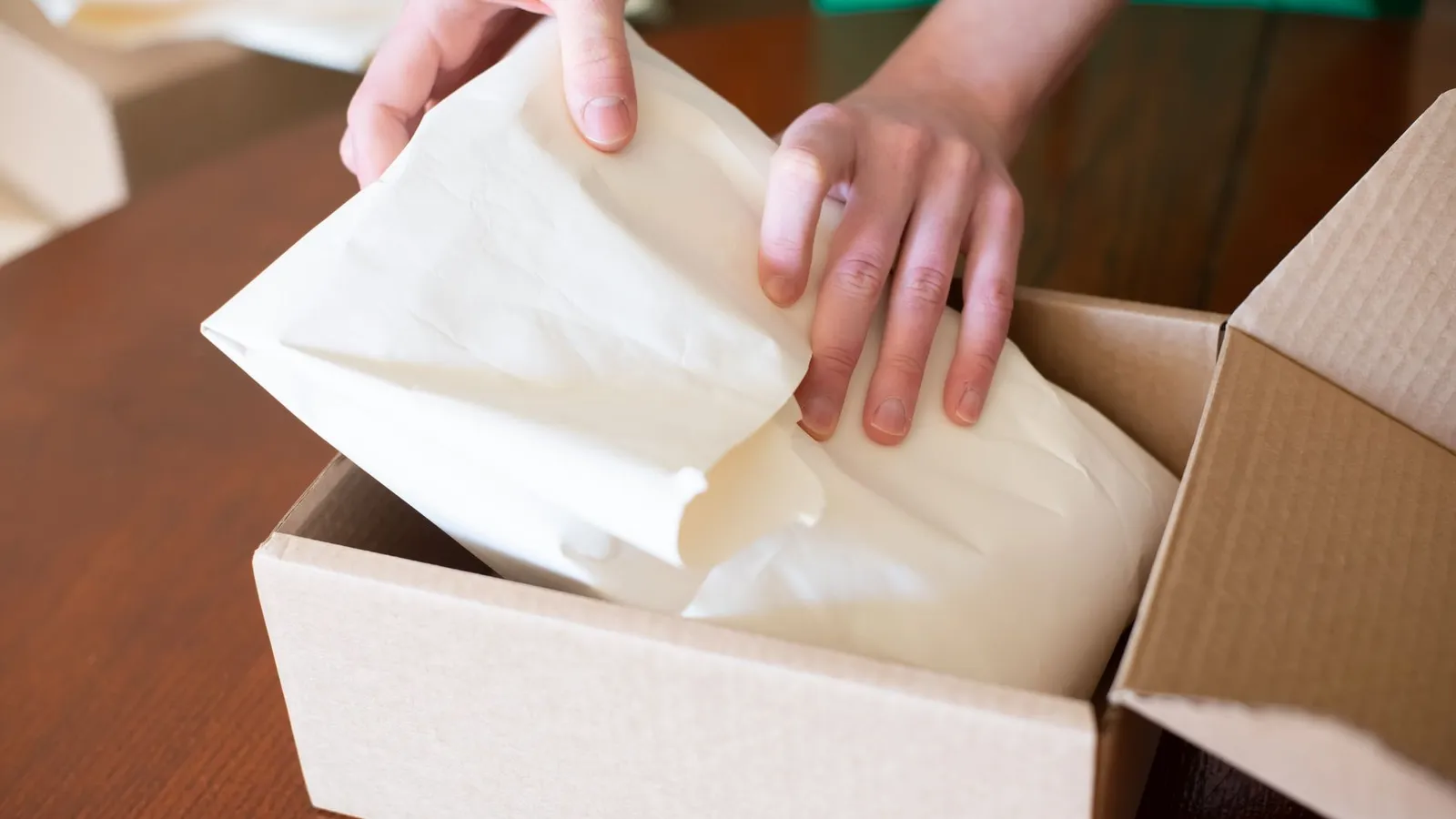 Mains emballant une commande dans un carton avant expédition, avec papier de calage