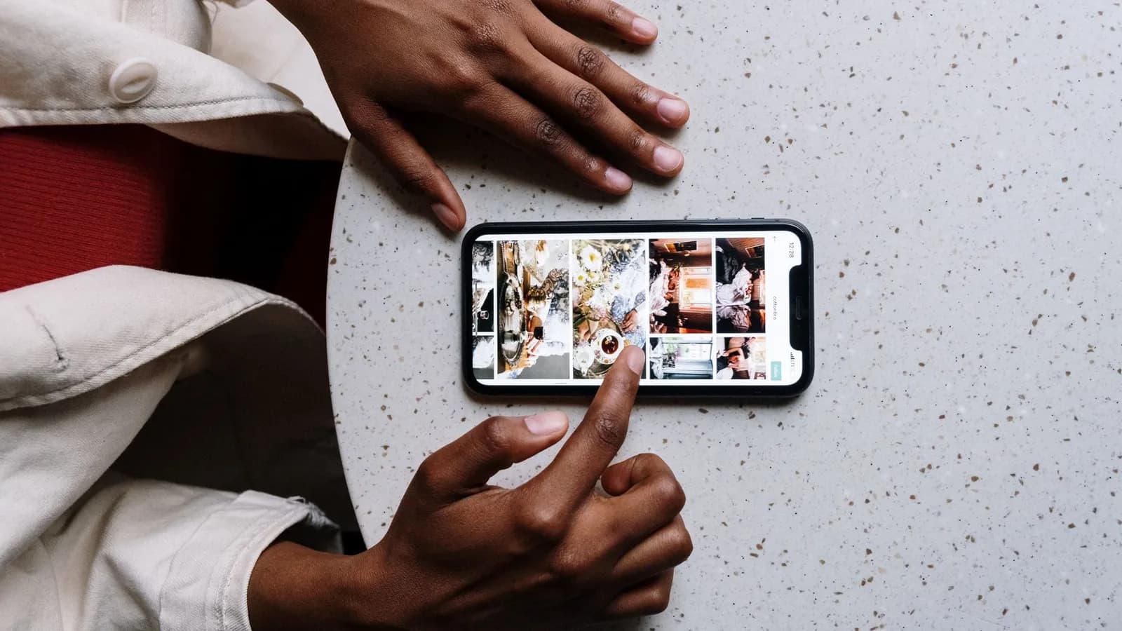 Mains faisant défiler un fil de publications sur un smartphone posé au-dessus d'une table de café